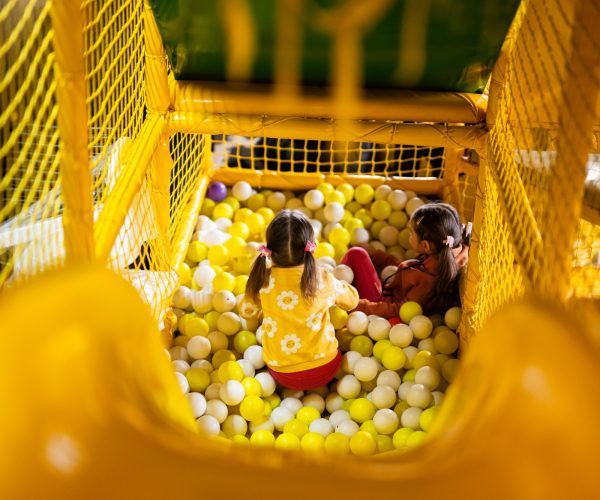 Siblings play with colored balls at yellow playground park. Sisters in active entertaiments.
